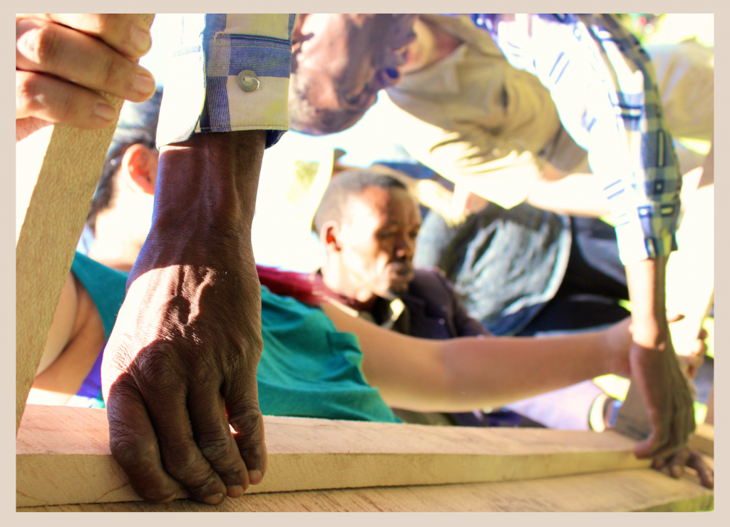 Image of a close-up of people’s hands who working together to assemble the wooden parts of an avocado dryer prototype in Leguruki, Tanzania.  